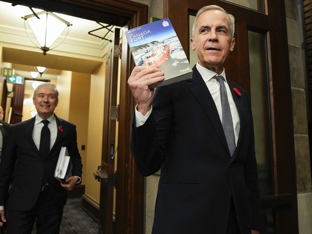 Prime Minister Mark Carney holds up a copy of the budget as he and Minister of Finance and National Revenue Francois-Philippe Champagne make their way to the House of Commons for the tabling of the federal budget on Parliament Hill in Ottawa, on Tuesday, Nov. 4, 2025.
