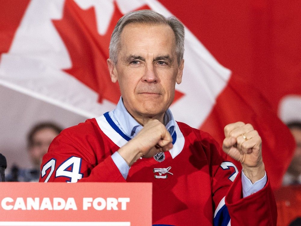 Mark Carney strikes a fighter's pose at a campaign rally while wearing a Montreal Canadiens jersey given to him by Liberal MP Marc Miller,  in Laval, north of Montreal Tuesday April 22, 2025.