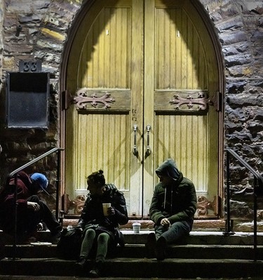 People sit in the cold outside of St. Barnabas Anglican Church in St. Catharines, Ont., on Nov. 12, 2025.