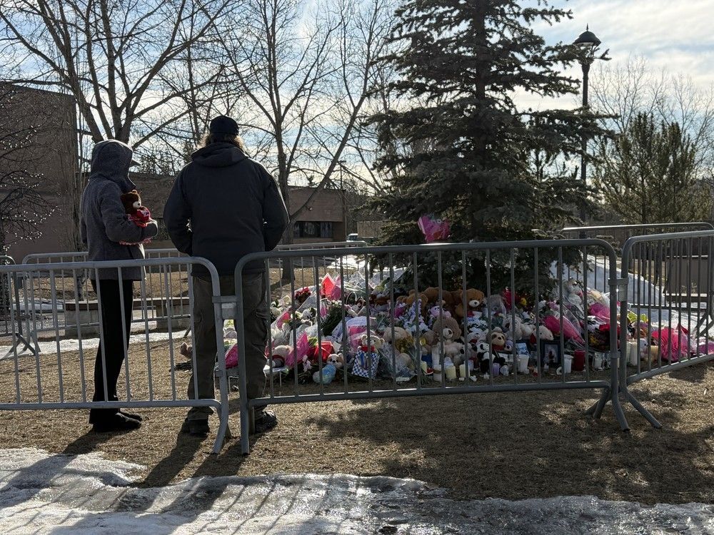 Mourners gather at a memorial with flowers set up to honour the shooting victims in Tumbler Ridge, B.C. on Friday, February 13, 2026.