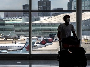 A person pushing a luggage trolley in an airport with the runway visible through a window in the background