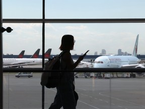 A woman wearing a backpack walks in front of a window at an airport with Air Canada planes visible in the background.