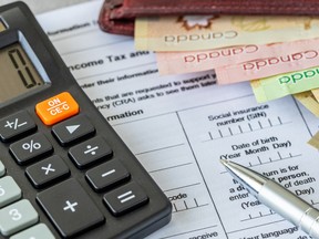 A calculator, pen and wallet with Canadian bank notes on top of a tax return form.