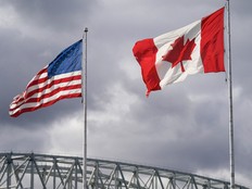 A Canadian and a U.S flag fly in front of a cloudy grey sky at the Blue Water Bridge border.