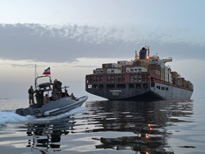 A small military boat following a cargo ship