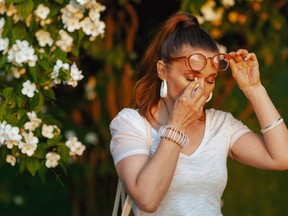 A woman holding a tissue to the corner of her eye while standing next to a flowering tree.