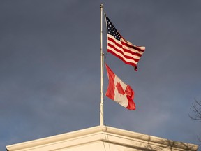 A US flag and Canadian flag flying on the same poll in front of a cloudy sky