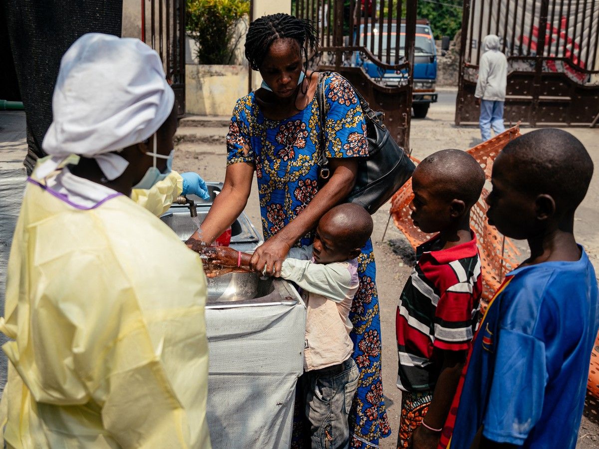 A mother helps her children wash their hands