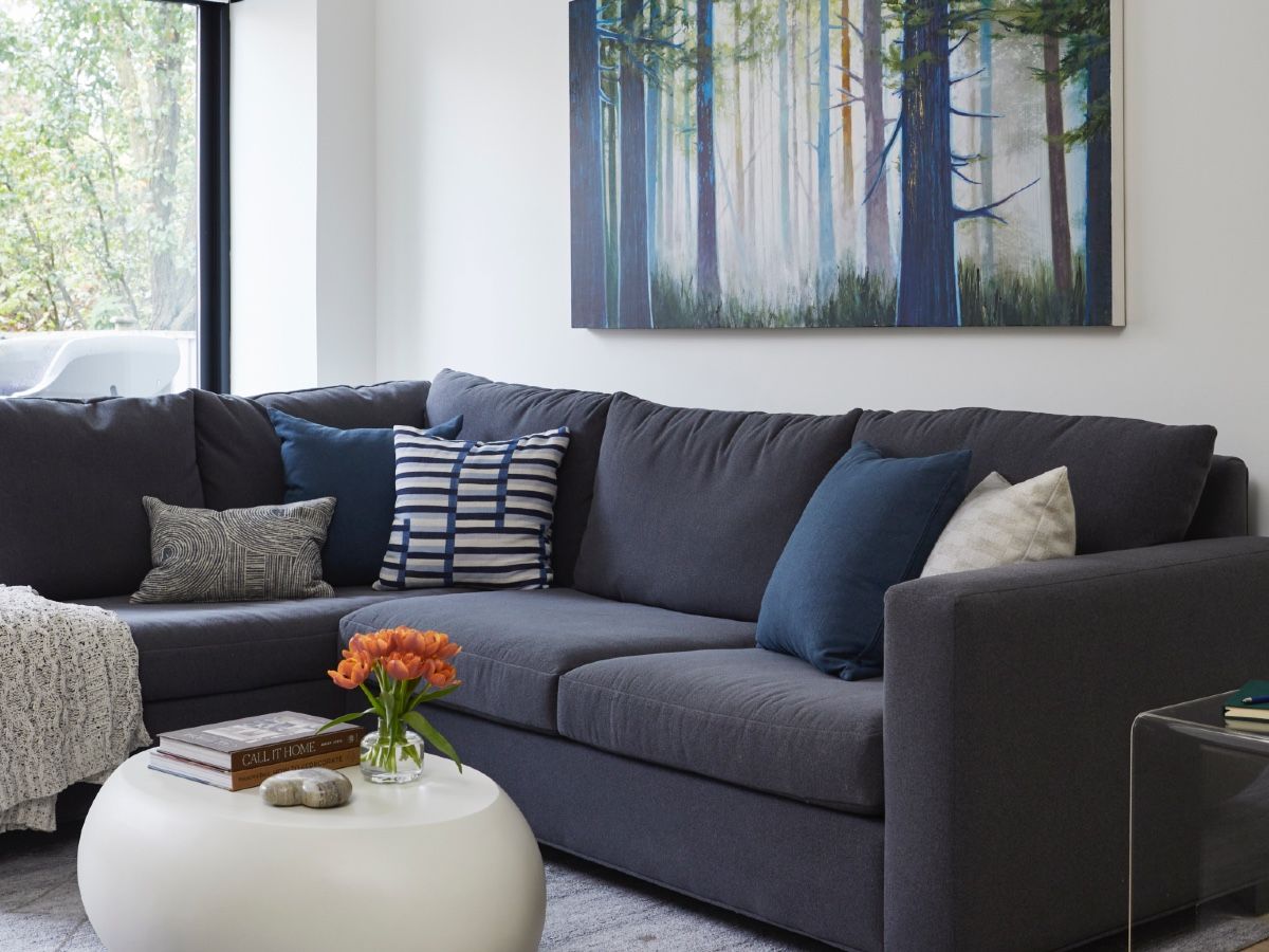 One of two Steven Nederveen works — a dreamlike forest scene — brings a nature-inspired colour story full circle in the living room. The charcoal sectional and sculptural pebble coffee table were custom ordered to fit the space.