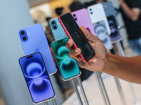 A row of iPhone 16s in an Apple store with a person holding one up in the foreground.