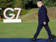 Trump walks along a blue carpet in front of a G7 sign.
