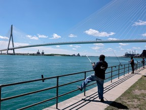 A person fishing next to a railing in front of a river with the Geordie Howe International Bridge in the background.