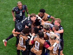 The Canada soccer team hug while on the pitch.