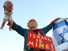 A person dressed up as Donald Trump and holding a baby puppet depicting Benjamin Netanyahu with a sign round their neck reading