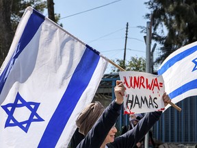 A woman holds an Israeli flag and a sign while protesting outside an UNRWA office in the West Bank.