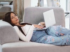 A woman lies on a couch with a laptop