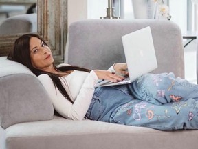 A woman lies on a couch with a laptop