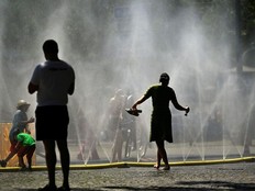 People walk through a water feature on a street on a sunny day.