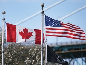 A Canadian flag and a U.S. flag fly next to each other under a blue sky.