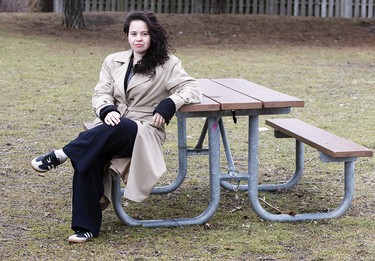 Lianne Wing-Martins wearing a beige coat and black trousers, sitting at a picnic bench with her legs crossed at Toronto’s Walter Saunders Memorial Park, Wednesday April 1, 2026