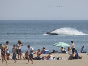 People sitting a walking along a sandy beach with the lake visible in the background.