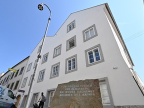 The front of a white building under a blue sky. In the foreground there is a stone with an inscription in German.