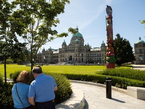 A couple look at a map in front of the Knowledge Totem carved by Master Carver Cicero August and his sons Darrell and Doug of the Cowichan Tribes on the front lawn of the B.C. legislature in Victoria, on Friday, May 22, 2026.