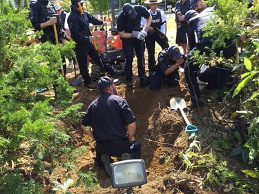 Members of the RCMP's forensic recovery team digging and gathered around a patch of earth.
