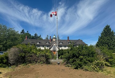 A flagpole with a Canadian flag at the top in front of an old building, under a blue sky.