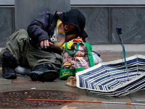A homeless man sits in the rain smoaking with a crack pipe in his hand in downtown Ottawa Friday morning