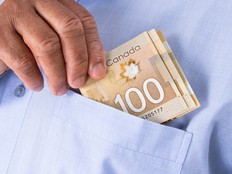 A close up of a man putting a $100 note into the breast pocket of a blue shirt.