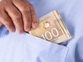 A close up of a man putting a $100 note into the breast pocket of a blue shirt.