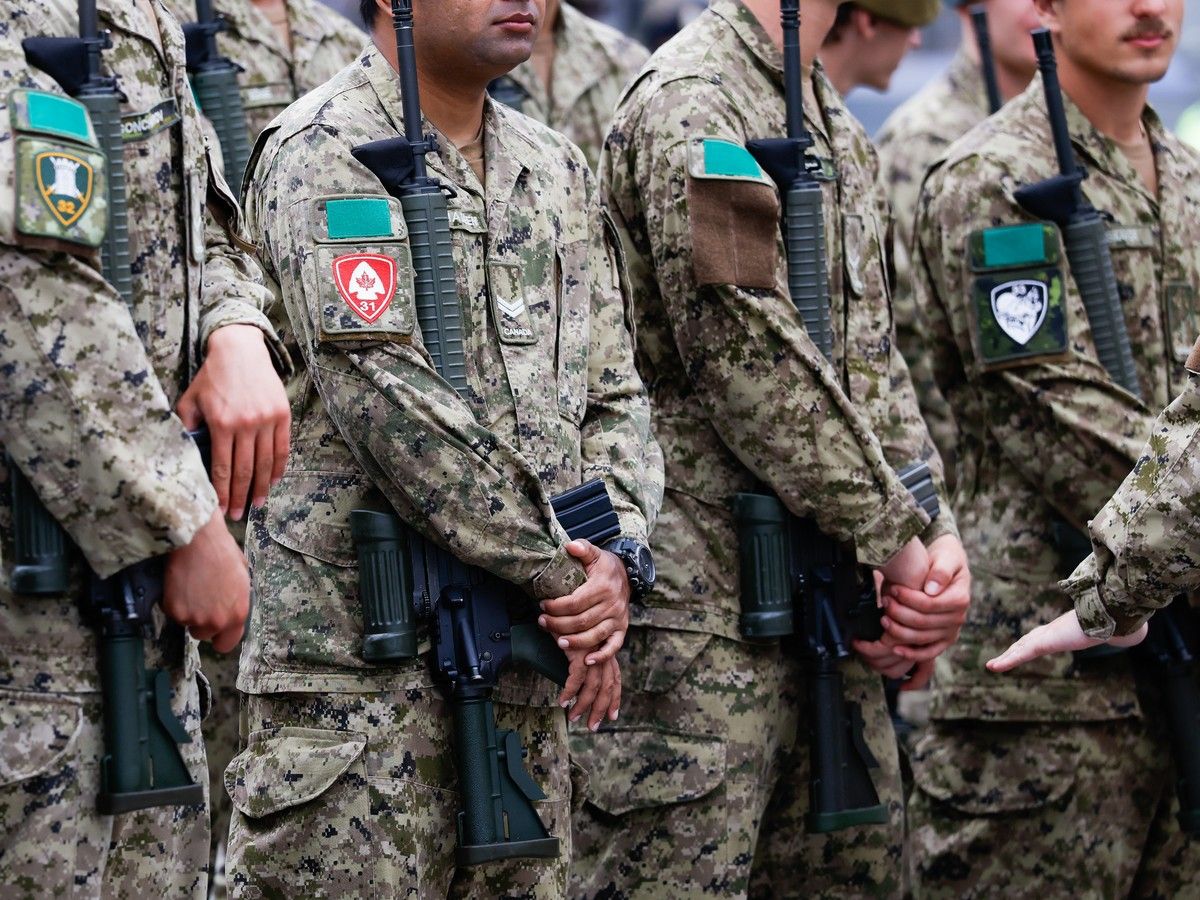 Members of Canadian Armed Forces in uniform stood in a line and each holding a rifle.