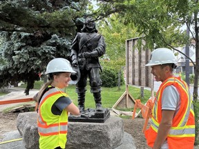 A statue of Samuel de Champlain in a park with two people wearing hi-vis and hard hats stood in front of it.
