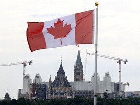 A Canadian flag with Parliament Hill in the background under a cloudy sky.