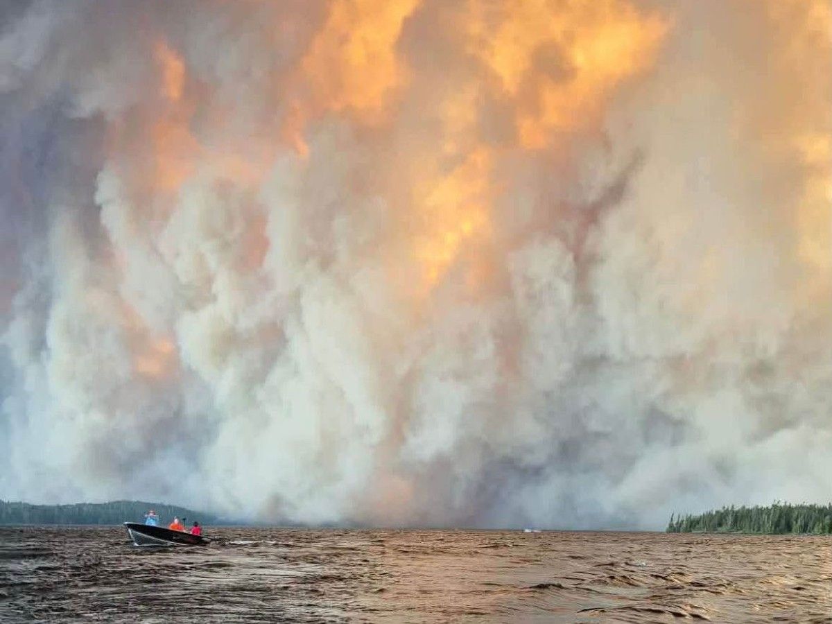 Members of Namaygoosisagagun First Nation flee by boat as a wildfire burns behind them. Every home in the community, about 250 kilometres north of Thunder Bay, was destroyed in Monday's fire. All of its members survived. Credit: Lyndon Paavola ( Kossak, Mason obtained permission from Matthew Hope to use image) Members of Namaygoosisagagun First Nation flee by boat as a wildfire burns behind them. Every home in the community, about 250 kilometres north of Thunder Bay, was destroyed in Monday's fire. All of its members survived. Credit: Lyndon Paavola ( Kossak, Mason obtained permission from Matthew Hope to use image)