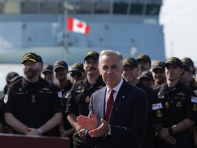 Mark Carney clapping with the Royal Canadian Navy behind him.