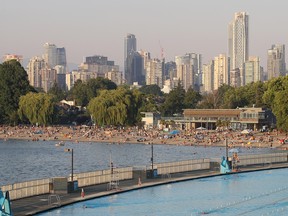 People crowded on Kitsilano Beach with the Vancouver skyline in the background.