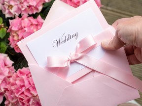 A pink paper wedding invitation with a pink ribbon around it and fpink flowers in the background.