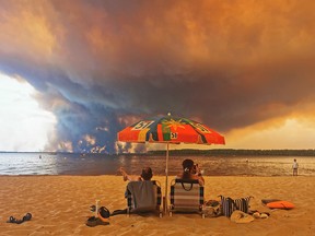 People on beach with wildfire in distance.