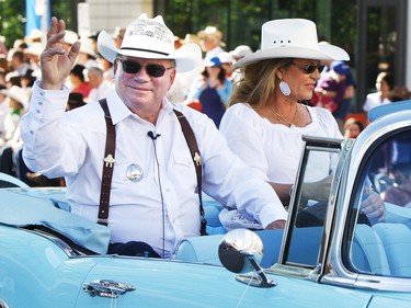 William Shatner, with his wife Elizabeth, wearing a white shirt and cowboy hat while waving from a blue open top car at the Calgary Stampede Parade.