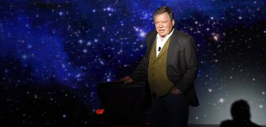 William Shatner performs his one-man show under a spotlight while wearing a three-piece suit.