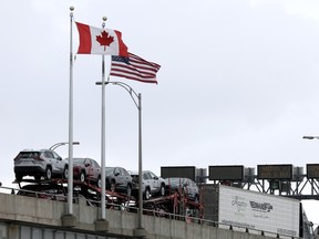 A truck crossing a bridge with a Canadian and a U.S. flag flying above.