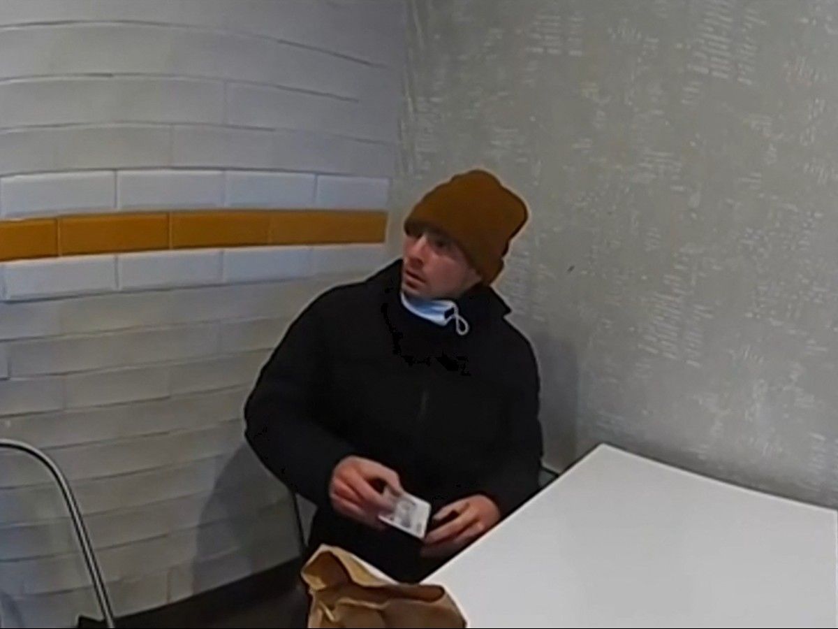Bodycam footage of Luigi Mangione wearing a coat and toque in a police station.
