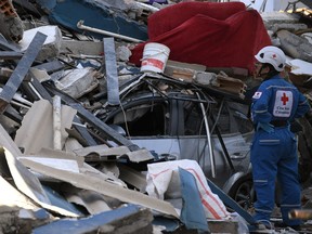 A person stands next to rubble on top of a car following an earthquake