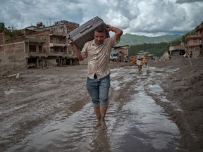A man carries a suitcase above his head while walking along a muddy road after a flood in Nepal.