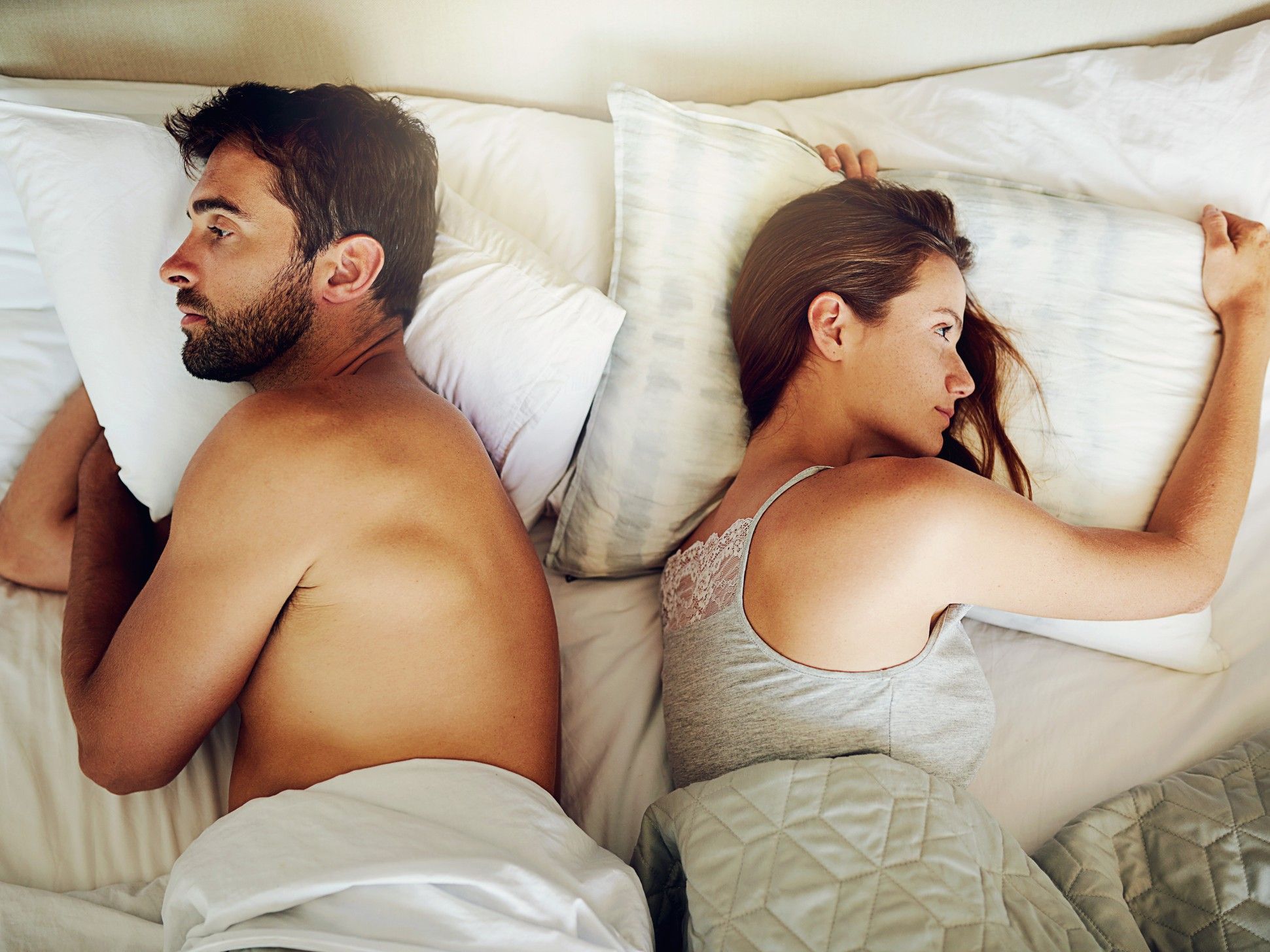 Couple lies in a bed backs to each other.