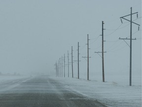 Empty road during a snowy winter with power line poles along the road.