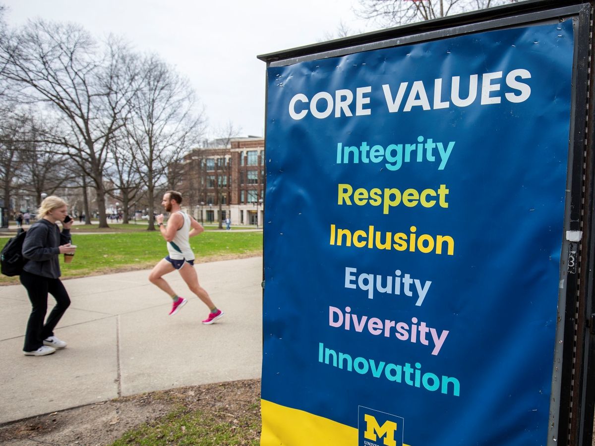 University of Michigan students walk on the UM campus next to signage displaying the University's