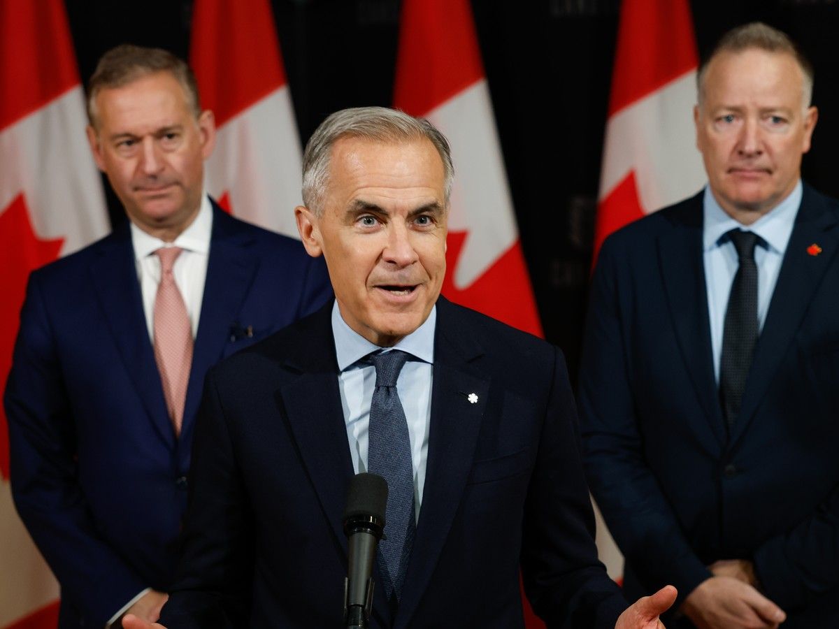 Doug Guzman and Stephen Fuhr look on while Mark Carney speaks at a podium